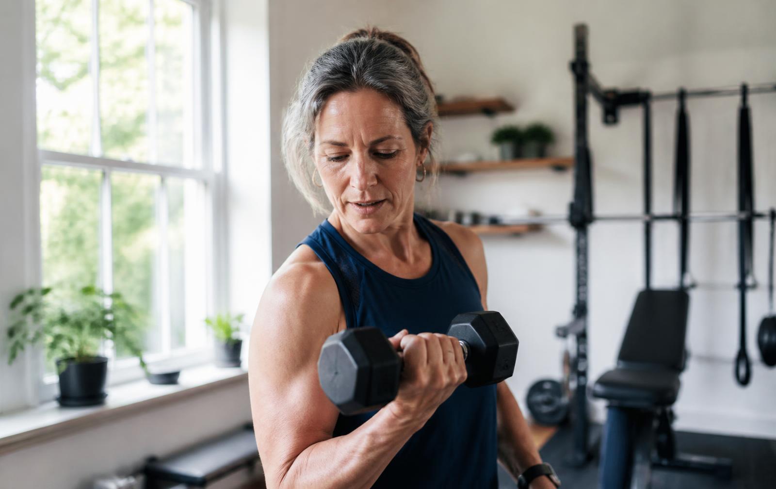 Woman in her fifties lifting a dumbbell in a bright home gym
