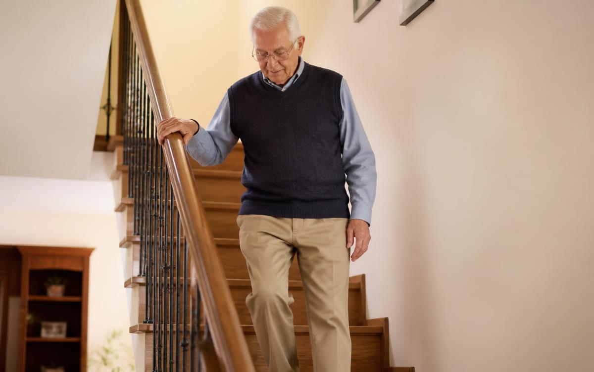 A senior man using a sturdy handrail while walking down interior stairs at home